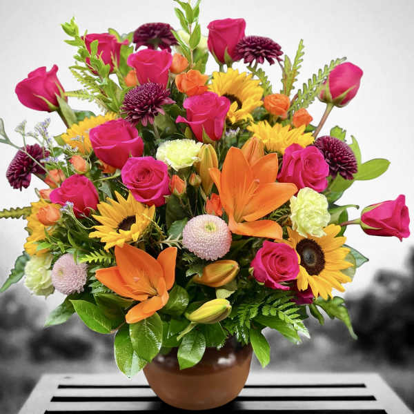 Colorful arrangement of pink roses, orange lilies, and yellow sunflowers in a terracotta pot