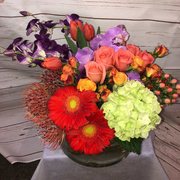 Colorful mixed bouquet with roses, orchids, gerbera daisies, and hydrangea in a glass vase