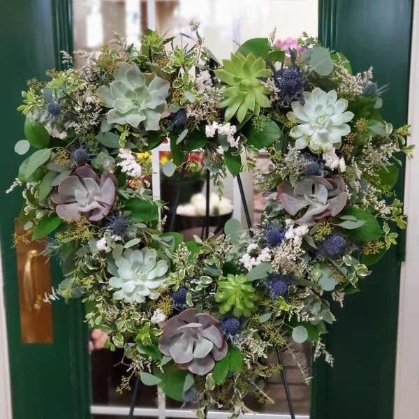 Heart-shaped succulent wreath on an easel with mixed greenery and blue accents