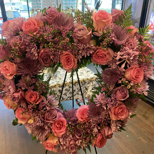 Heart-shaped floral wreath with pink and purple roses on a stand