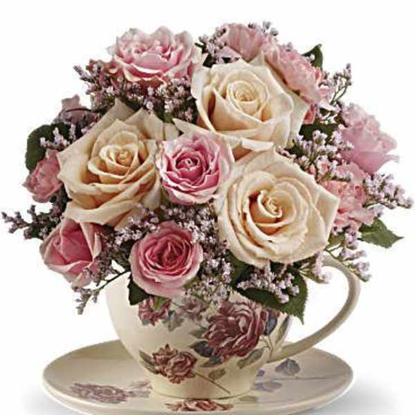 Pink and cream roses arranged in a floral teacup with saucer
