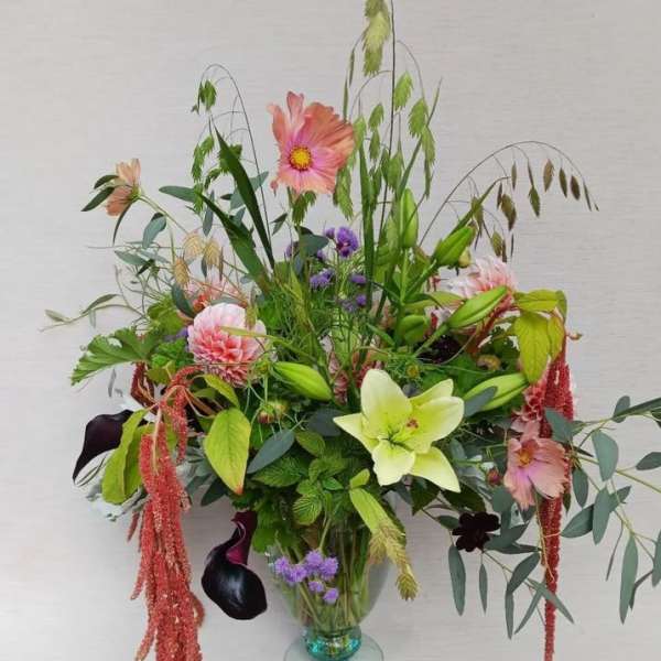 Tall garden-style arrangement with pink dahlias, green lily, dark calla lilies in a clear glass vase