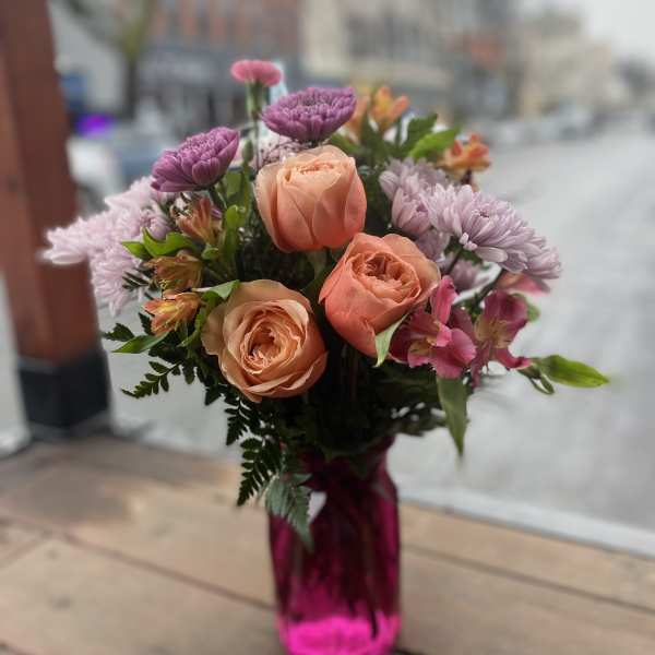 Bouquet of peach roses and purple flowers in a pink glass vase