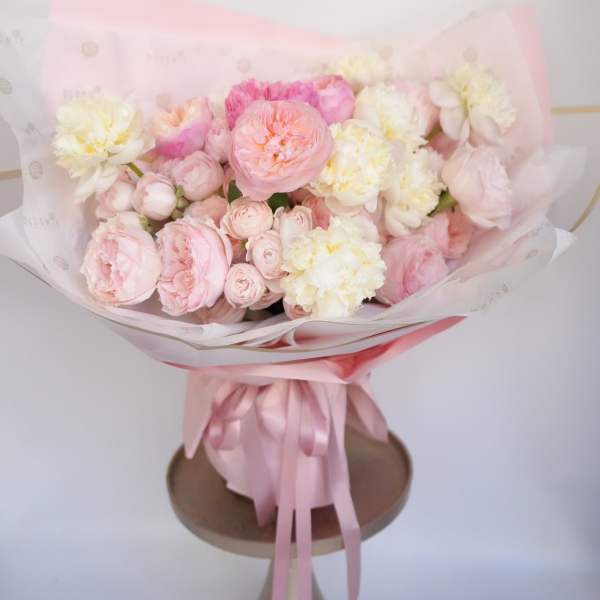 Round bouquet of pale pink and cream roses and peonies in a pink hatbox with ribbon