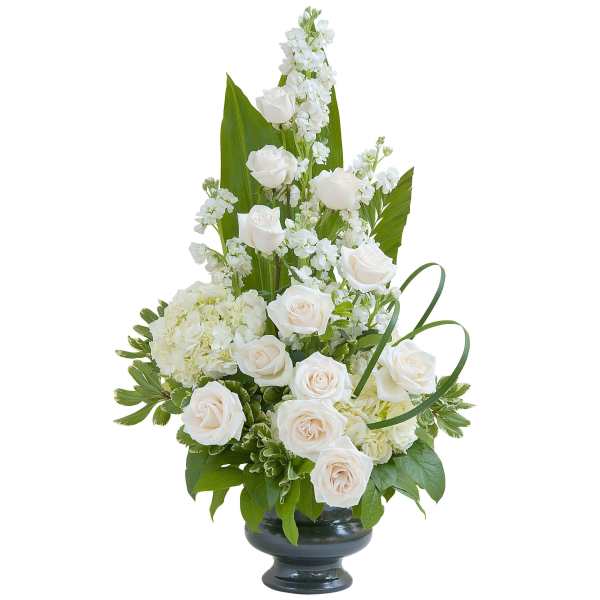 Tall arrangement of white roses, stock, and hydrangeas in a black pedestal vase