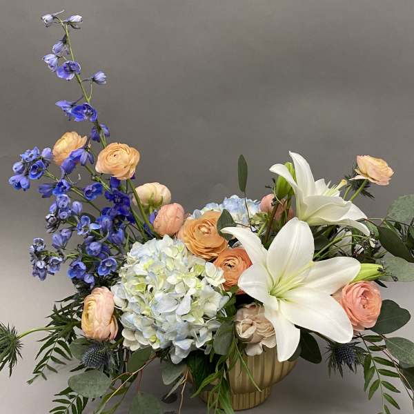 Mixed bouquet with white lilies, blue delphinium, peach ranunculus, and pale hydrangea