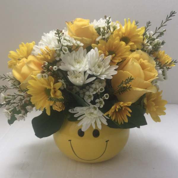 Yellow and white flower arrangement in a smiley-face container