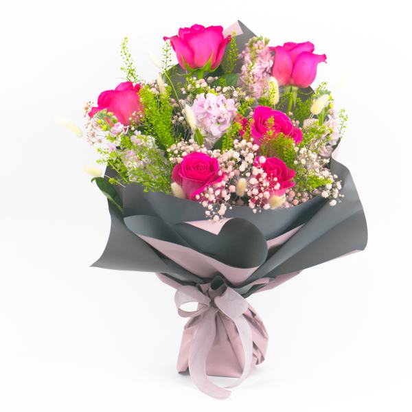 Bouquet of pink roses with small filler flowers wrapped in dark paper