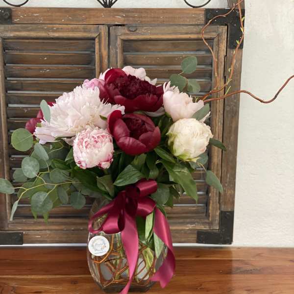 Bouquet of pink and burgundy peonies in a glass vase with a ribbon