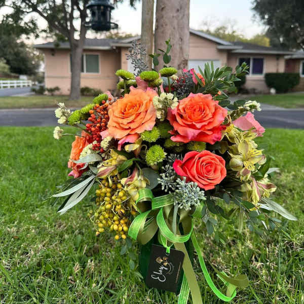 Bouquet of orange and coral roses with green accents and ribbon