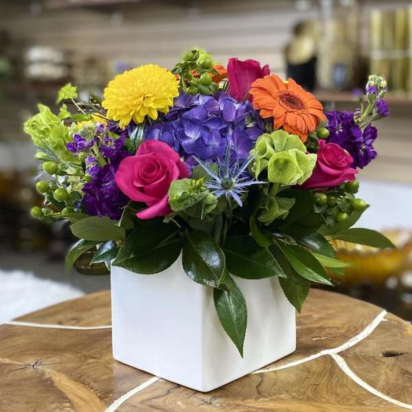 Colorful mixed flower arrangement in a white square vase