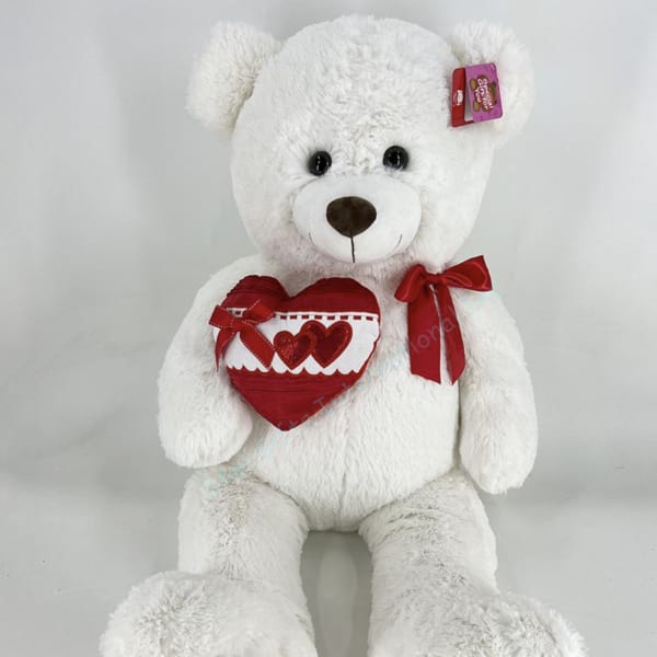 White teddy bear holding a red heart and wearing a red ribbon