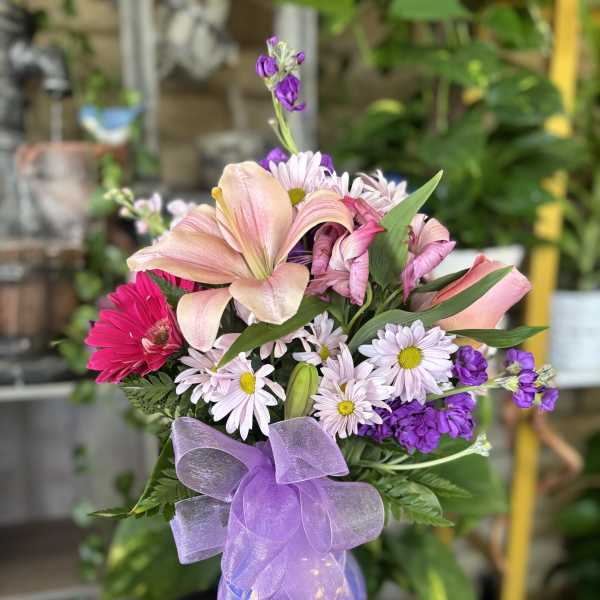Pink and purple mixed bouquet in a lavender vase with a sheer bow