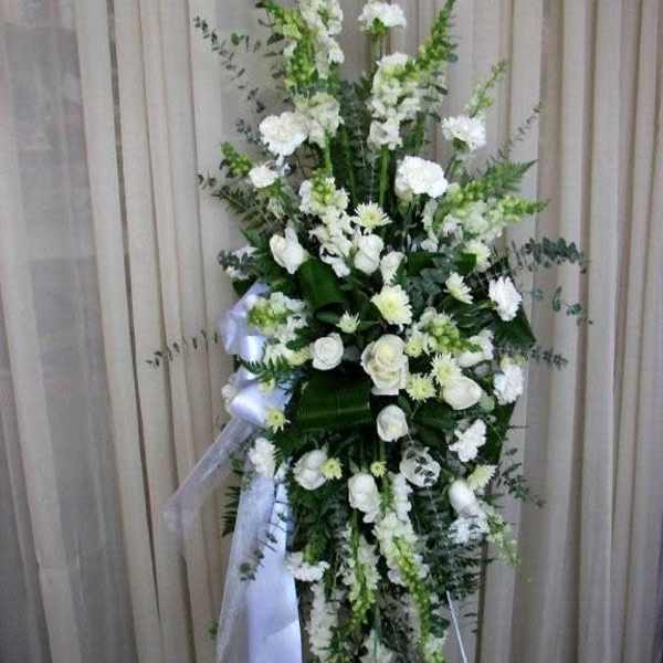 Tall white floral standing spray with ribbon on an easel