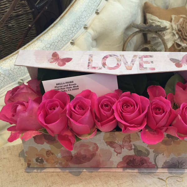 Pink roses arranged in a floral gift box with a LOVE lid