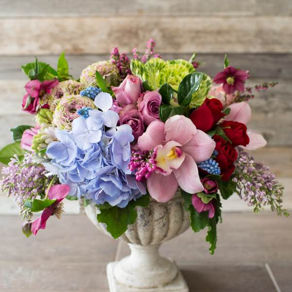 Mixed bouquet of pink, blue, red, and green flowers in a white pedestal vase