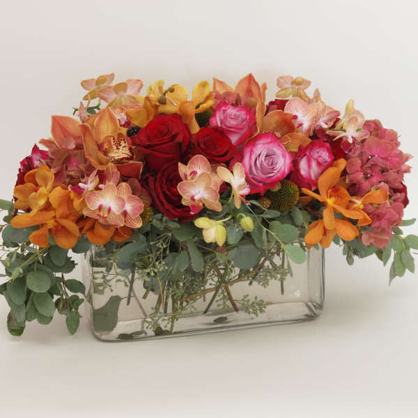 Mixed bouquet of roses and orchids in a clear rectangular vase