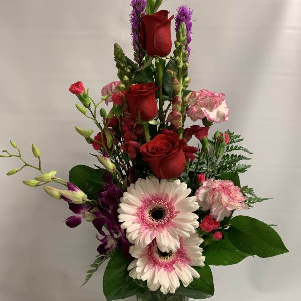 Tall bouquet of red roses, pink gerberas, and purple orchids in a glass vase