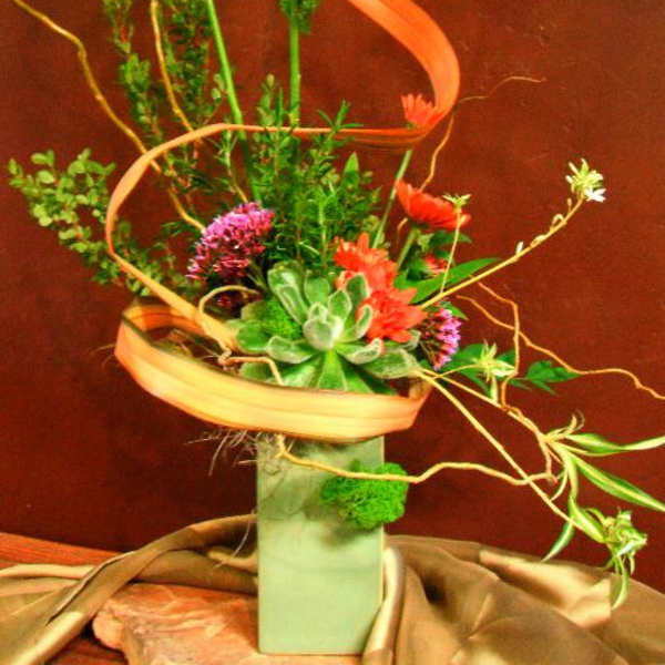 Tall floral arrangement with orange blooms in a square vase