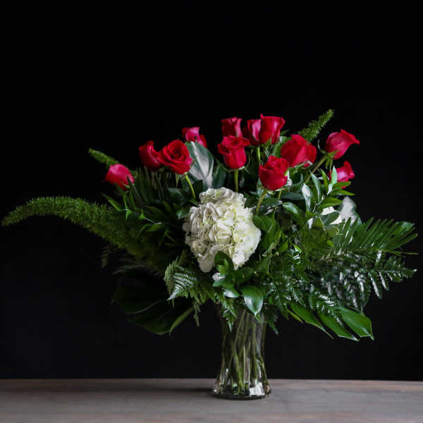 Tall arrangement of red roses and white hydrangea in a clear glass vase