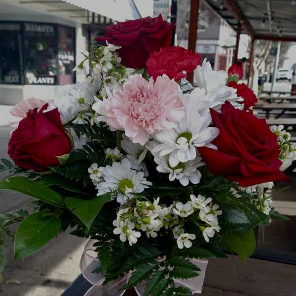 Bouquet of red roses, pink carnations, and white daisies in a red vase