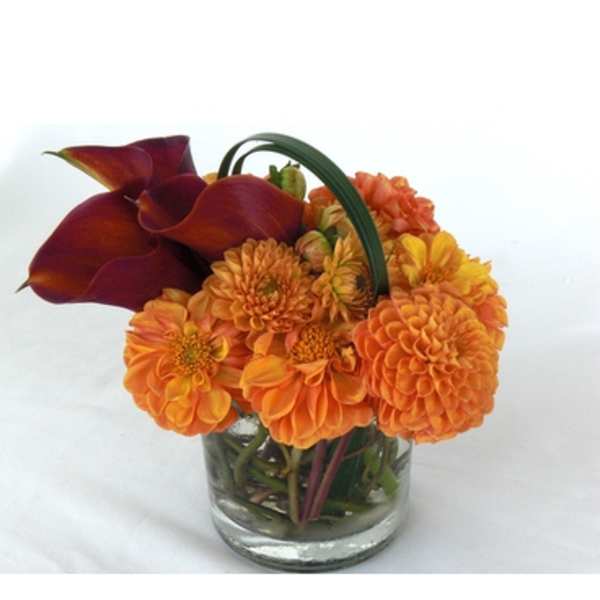 Orange flowers and dark calla lilies in a clear glass vase
