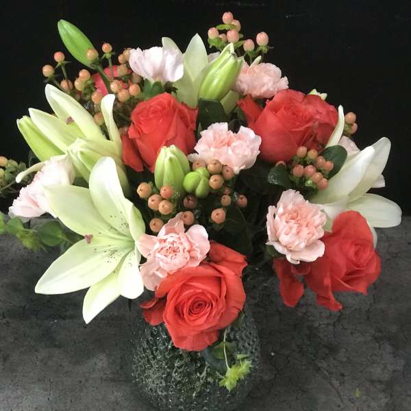 Bouquet of red roses, white lilies, and pink carnations in a glass vase