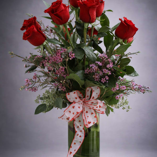 Red roses in a glass vase with a heart-patterned ribbon
