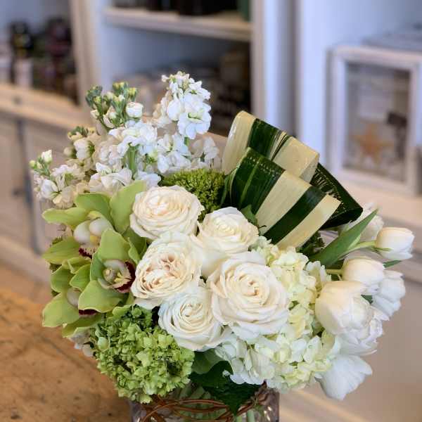 White roses and green orchids arranged in a square glass vase