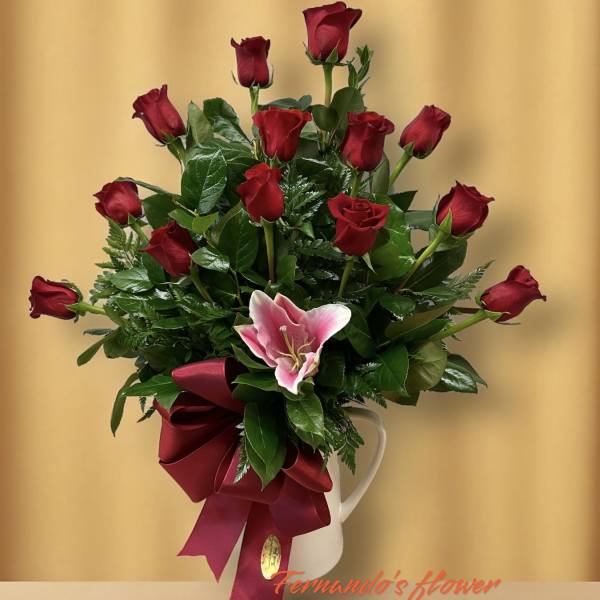 Tall arrangement of red roses with a pink lily and red bow in a white pitcher vase