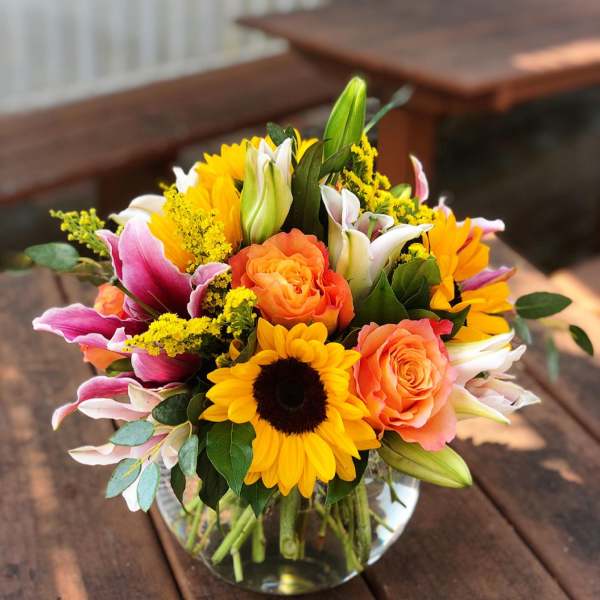 Bouquet of sunflowers, orange roses, and pink lilies in a glass vase