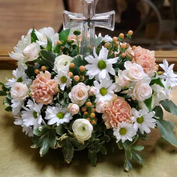 Floral arrangement with a clear cross centerpiece, white daisies, pale roses, and peach carnations