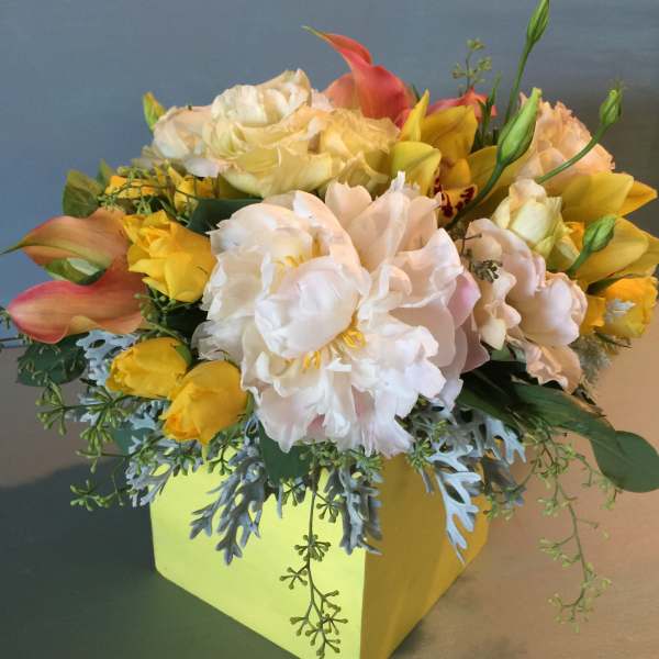 Yellow and white floral arrangement in a square box with pink calla lilies