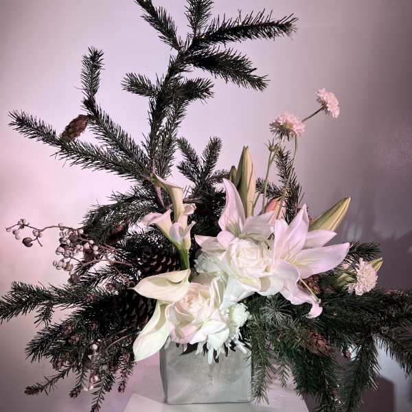 White lilies and roses arranged with pine branches in a square vase