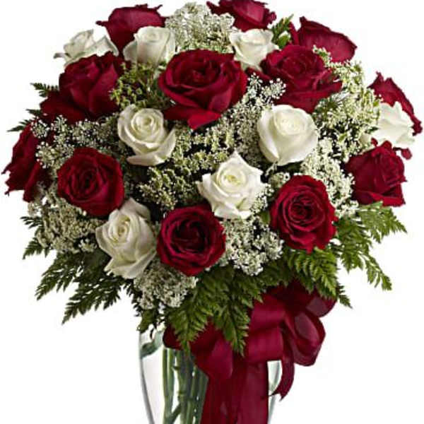 Arrangement of red and white roses in a clear glass vase with a red ribbon bow.