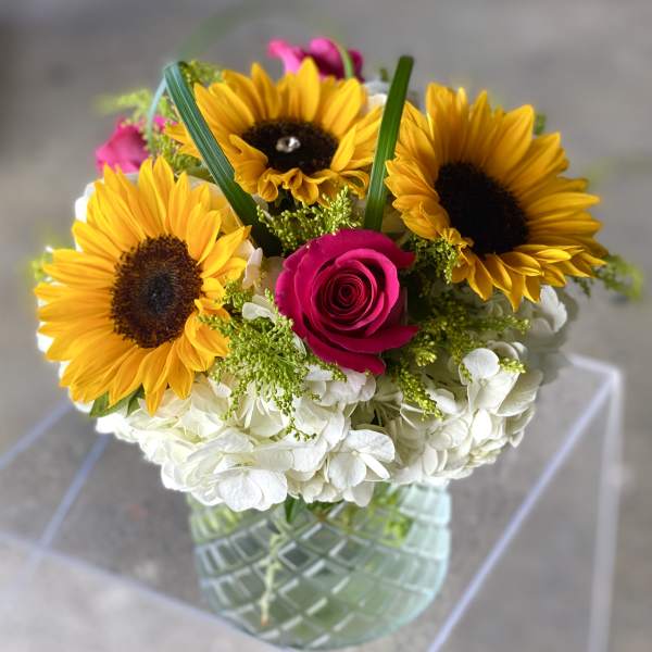 Bouquet of sunflowers, a pink rose, and white hydrangeas in a glass vase