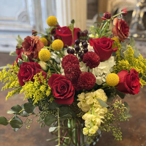 Bouquet of red roses, yellow billy balls, and mixed blooms in a glass vase