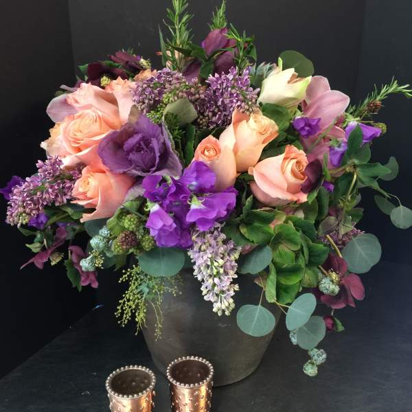 Mixed bouquet of peach roses and purple flowers in a dark vase