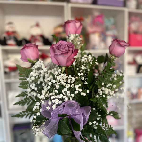 Pink roses in a glass vase with baby's breath and a purple ribbon
