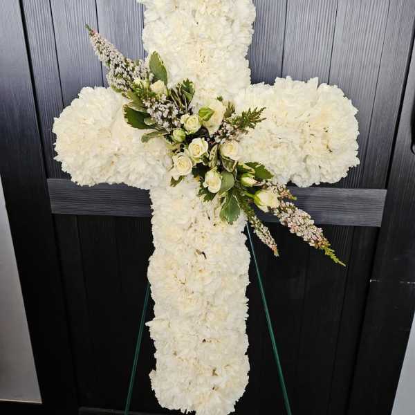 White floral cross on an easel with small roses and greenery at the center
