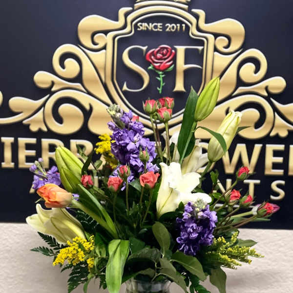 Mixed bouquet of lilies, roses, and purple flowers in a glass vase