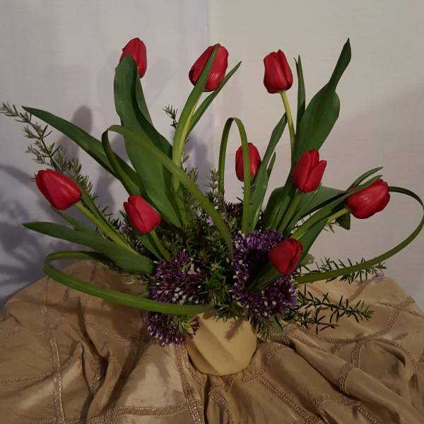Red tulips arranged in a beige vase with purple filler flowers
