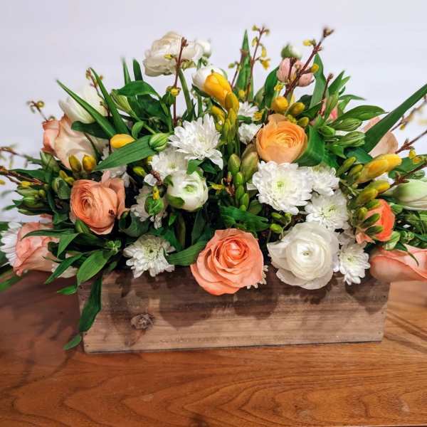 Low arrangement of peach, white, and yellow flowers in a rustic rectangular wooden box