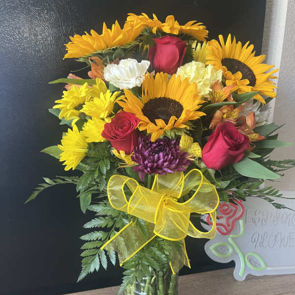 Bouquet of sunflowers, red roses, and mixed blooms in a glass vase
