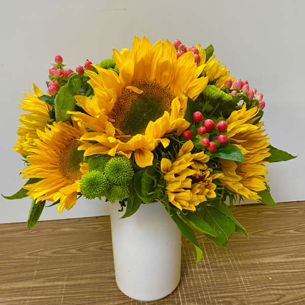 Sunflower bouquet in a white vase with pink berries and green button mums