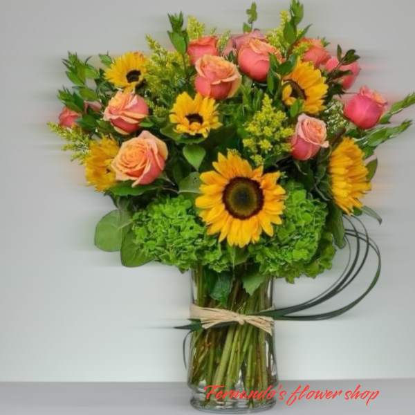 Vase arrangement of yellow sunflowers and pink roses with green hydrangeas in a clear glass cylinder