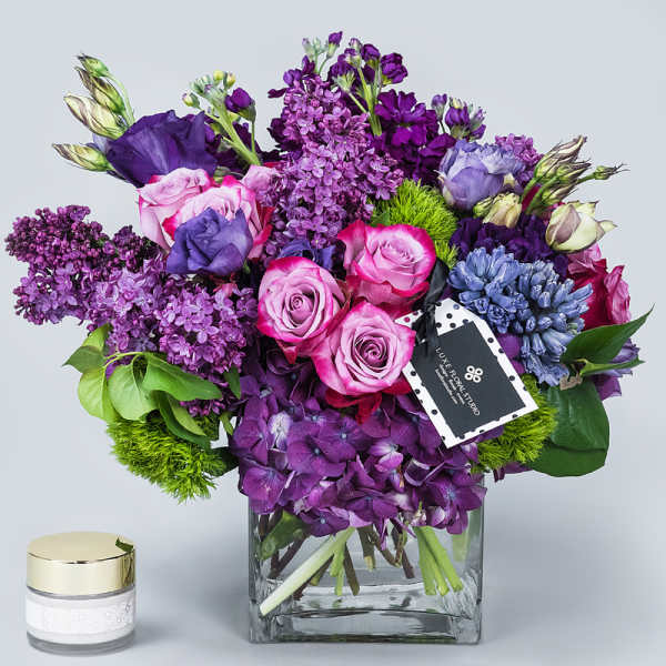 Purple and pink bouquet in a square glass vase with a small candle beside it
