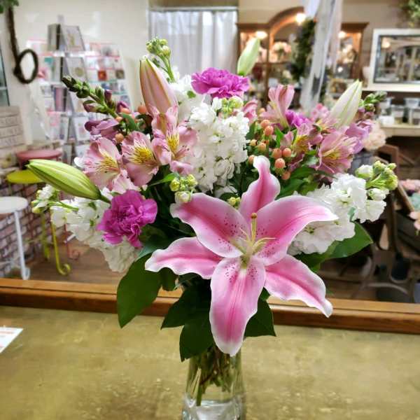 Pink lilies and mixed flowers arranged in a clear glass vase