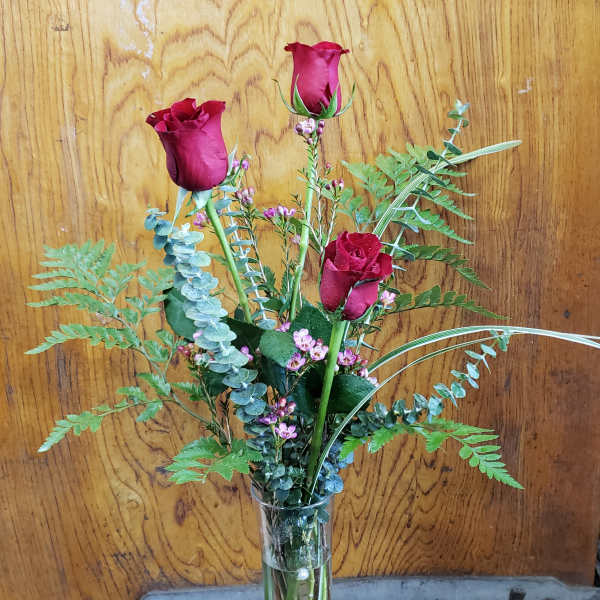 Three red roses in a clear glass vase with airy greenery