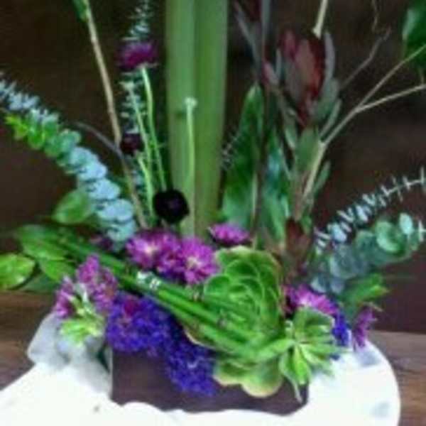 Tall tropical floral arrangement with purple blooms in a white container